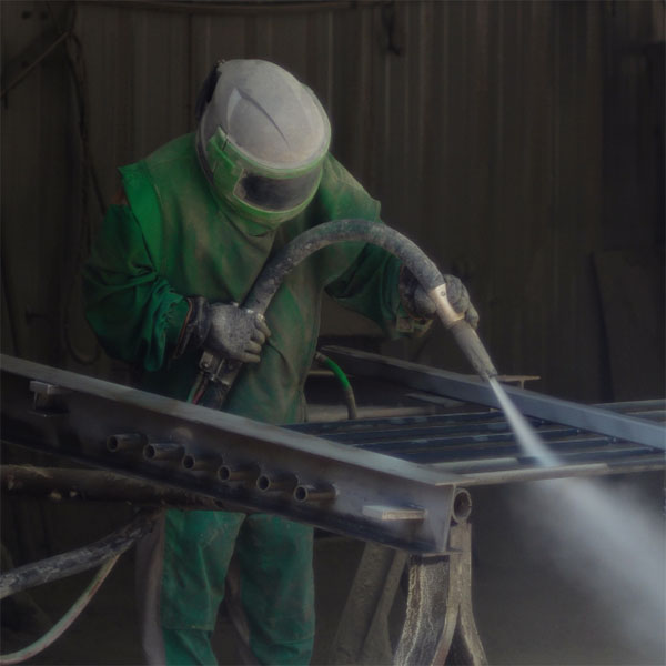 Skilled worker in full safety gear sandblasting a metal component at Renfrow+Co highlighting their metal finishing and fabrication expertise