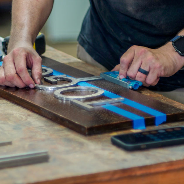 Renfrow+Co craftsman assembling custom signage showcasing metal and wood integration for unique design projects in Houston