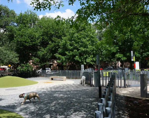 Playground area at Levy Park featuring a custom fabricated metal fence with shaded green spaces and recreational equipment in the background