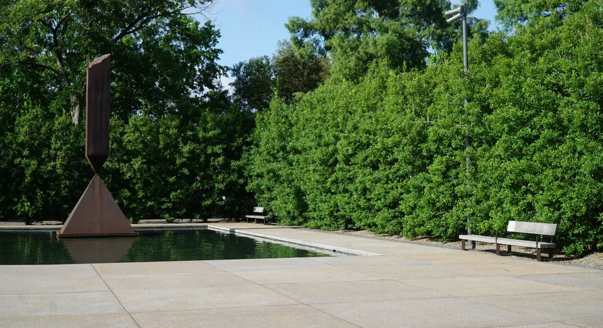 Reflecting pool and sculpture at Rothko Chapel, with a Renfrow+Co-crafted wooden bench placed along the tree line