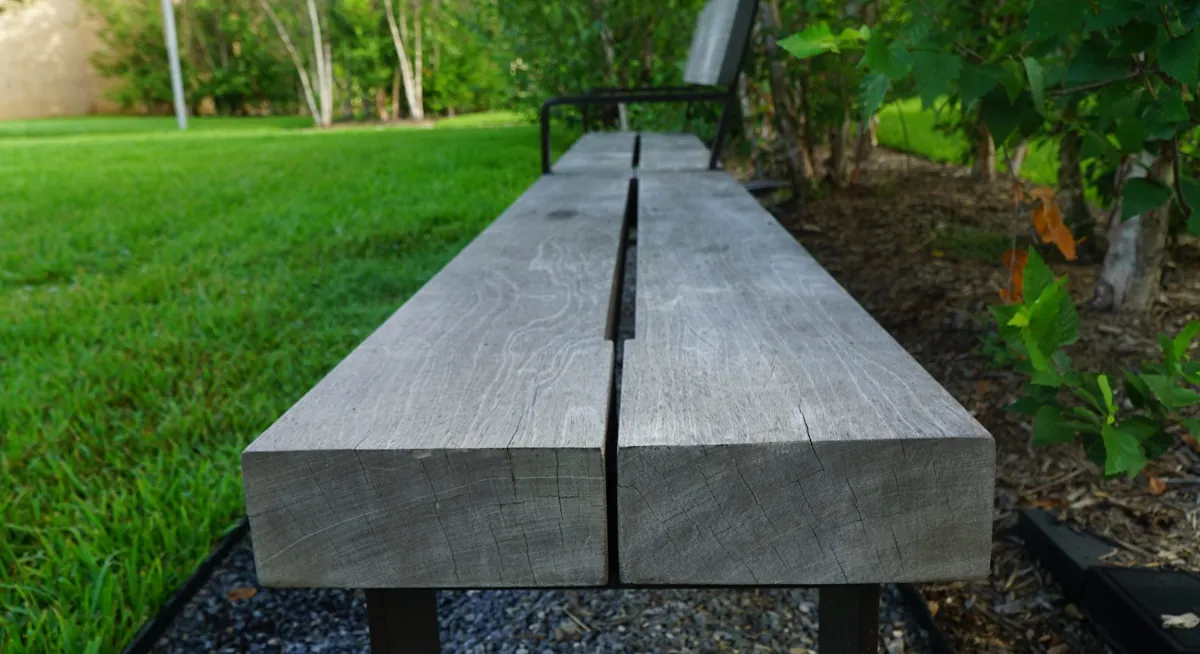 Detailed shot of a wooden bench with metal armrests, carefully refurbished by Renfrow+Co, set against the peaceful backdrop of Rothko Chapel gardens
