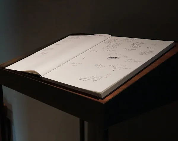 Close-up of a guestbook on a custom-built wooden stand crafted by Renfrow+Co for Rothko Chapel, with signatures and messages written by visitors