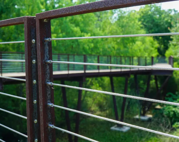 Close-up of weathered steel railing with cable rail design by Renfrow+Co, framing the elevated wooden walkway of the High Island Sky Walk Close-up of weathered steel railing with cable rail design by Renfrow+Co, framing the elevated wooden walkway of the High Island Sky Walk