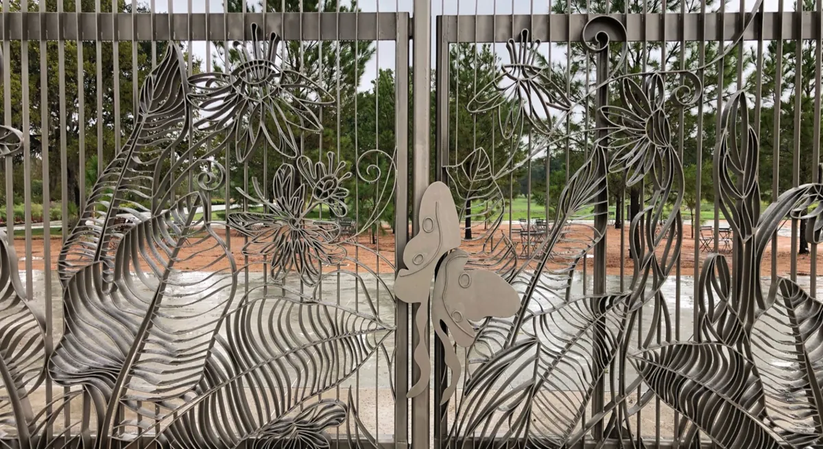 Custom metal gate crafted by Renfrow+Co, featuring intricate botanical patterns and a butterfly detail at the Houston Botanic Garden Custom metal gate crafted by Renfrow+Co, featuring intricate botanical patterns and a butterfly detail at the Houston Botanic Garden
