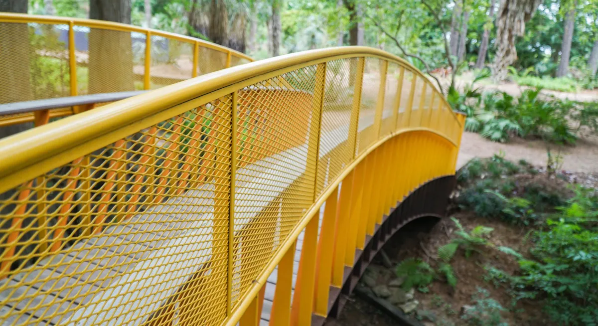 Renfrow+Co expertly fabricated this bridge railing, featuring a striking combination of yellow stainless steel mesh and a sturdy Ipe wood walkway, in John Fairey Garden Renfrow+Co expertly fabricated this bridge railing, featuring a striking combination of yellow stainless steel mesh and a sturdy Ipe wood walkway, in John Fairey Garden